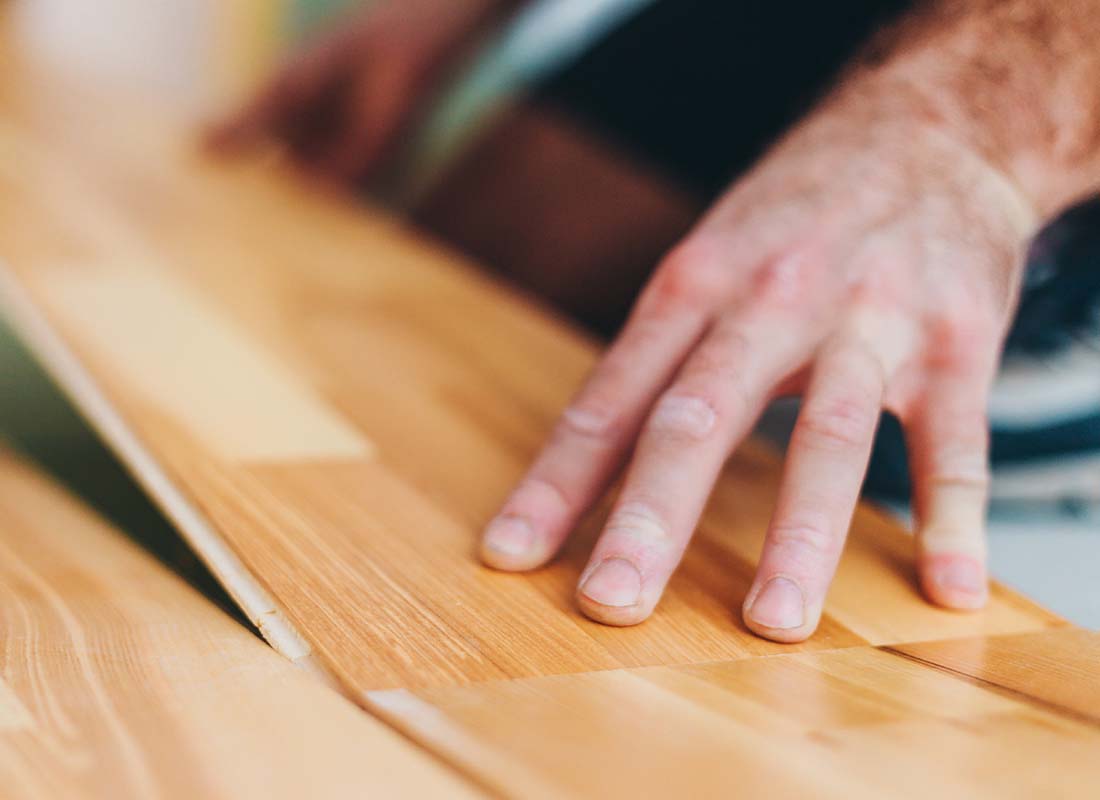 Flooring Contractor Insurance - Close-up of a Carpenter Skillfully Installing and Connecting the Panels of Parquet Floating Floor in a New Home