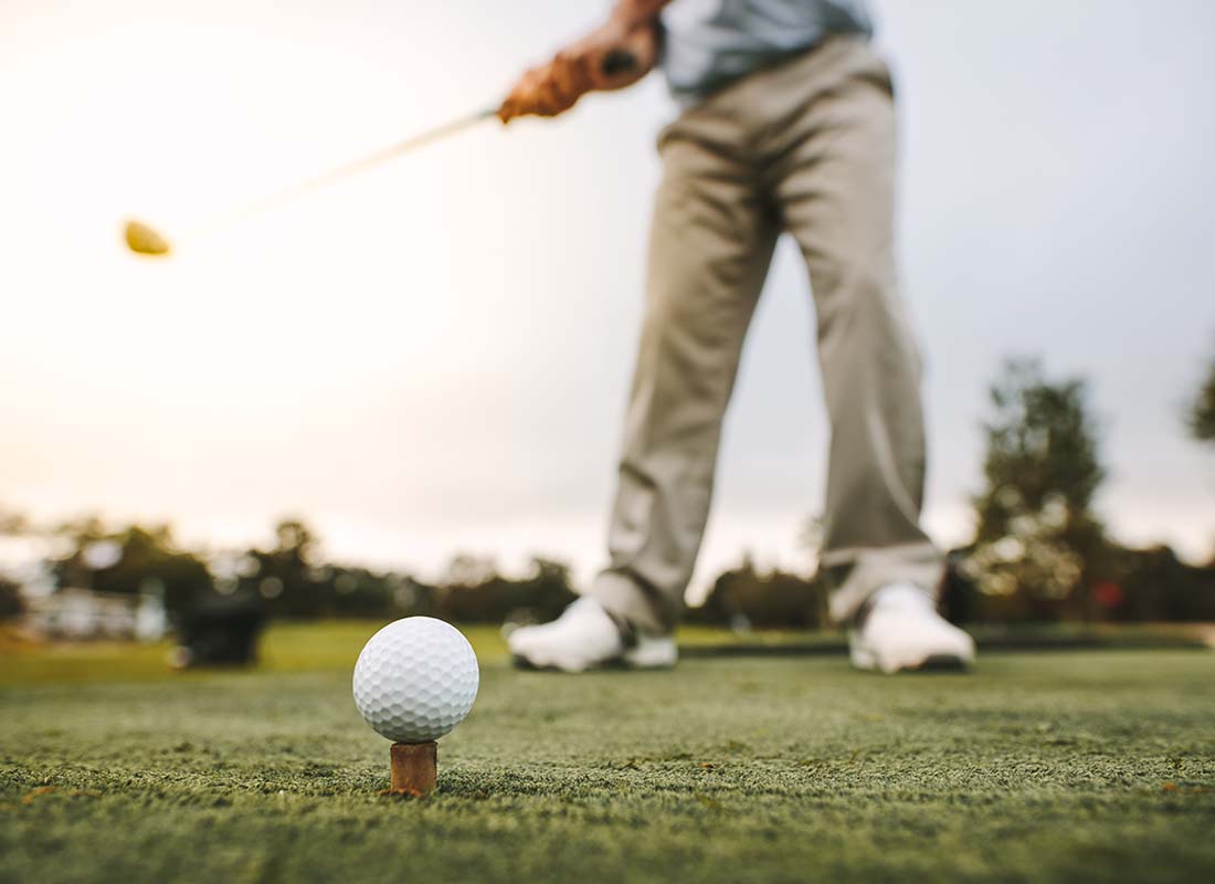 Golf Course Insurance - Close-up of the Bottom Half of a Golfer Taking a Swing at the Golf Course Driving Range on a Summer Day at Dusk