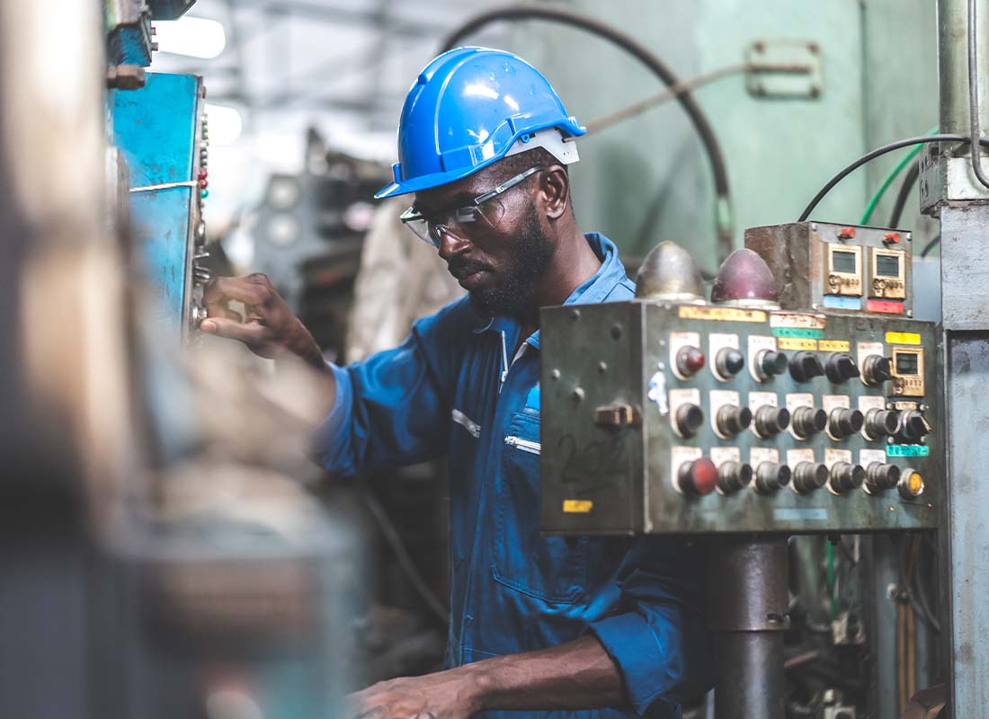 Machine Shop Insurance - Male Engineer Working on a Laptop Computer in Machine Factory and Checking Quality Control and the Condition of the Machine