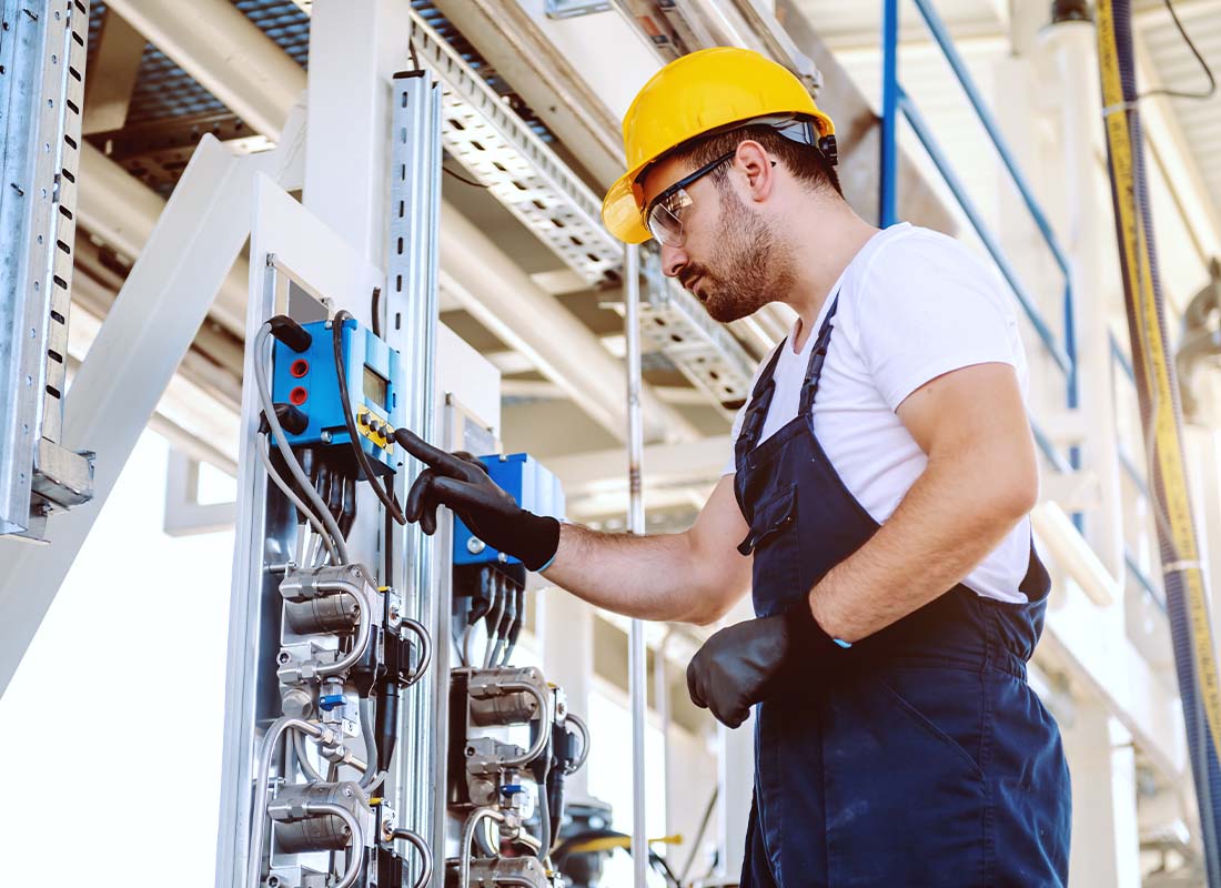 Oil and Gas Insurance - Side View of Worker in Overalls and Yellow Helmet Pressing Button on a Dashboard to Monitor Oil Production in an Oil and Gas Refinery